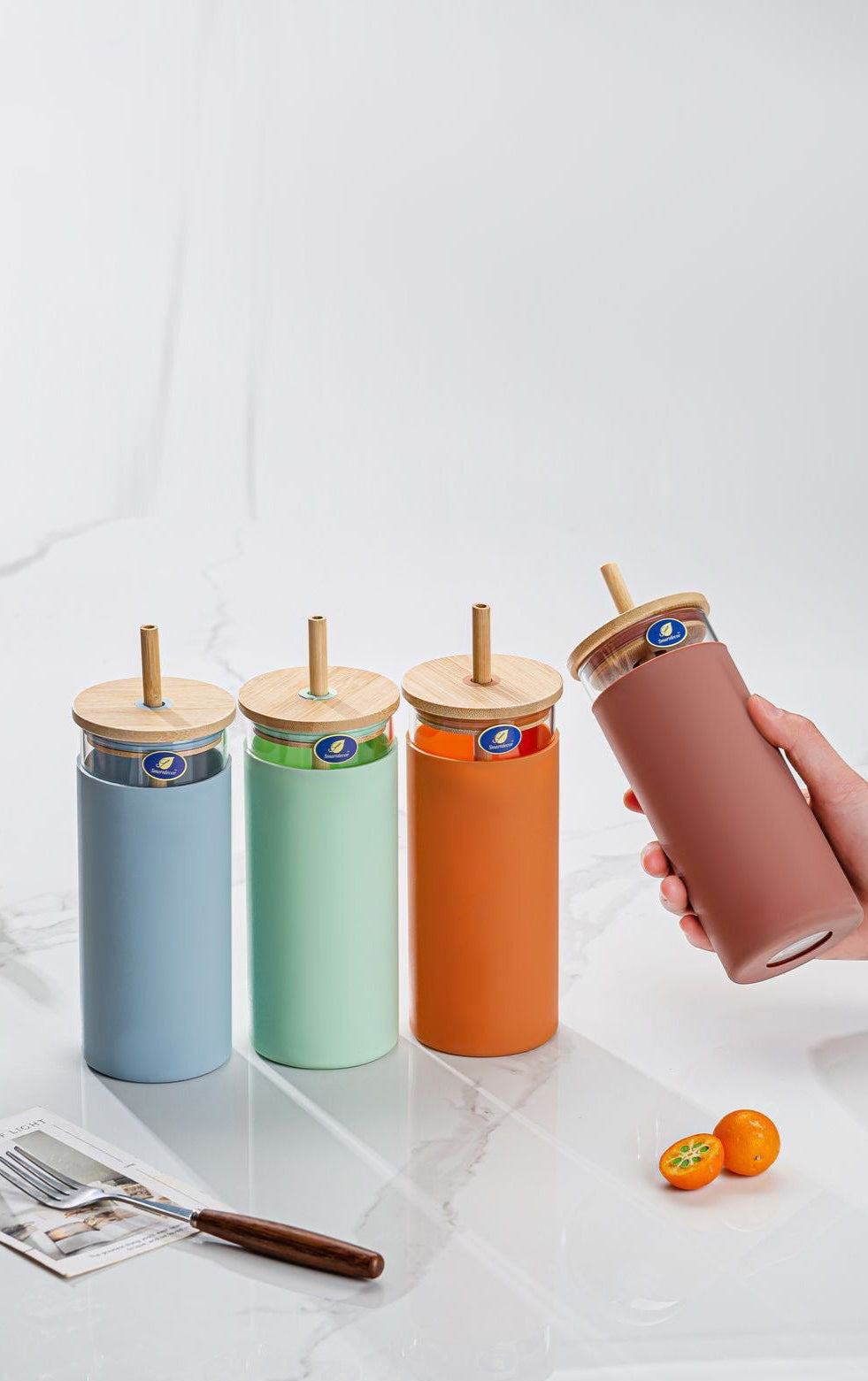 Set of colorful tumblers with wooden lids on a marble surface.