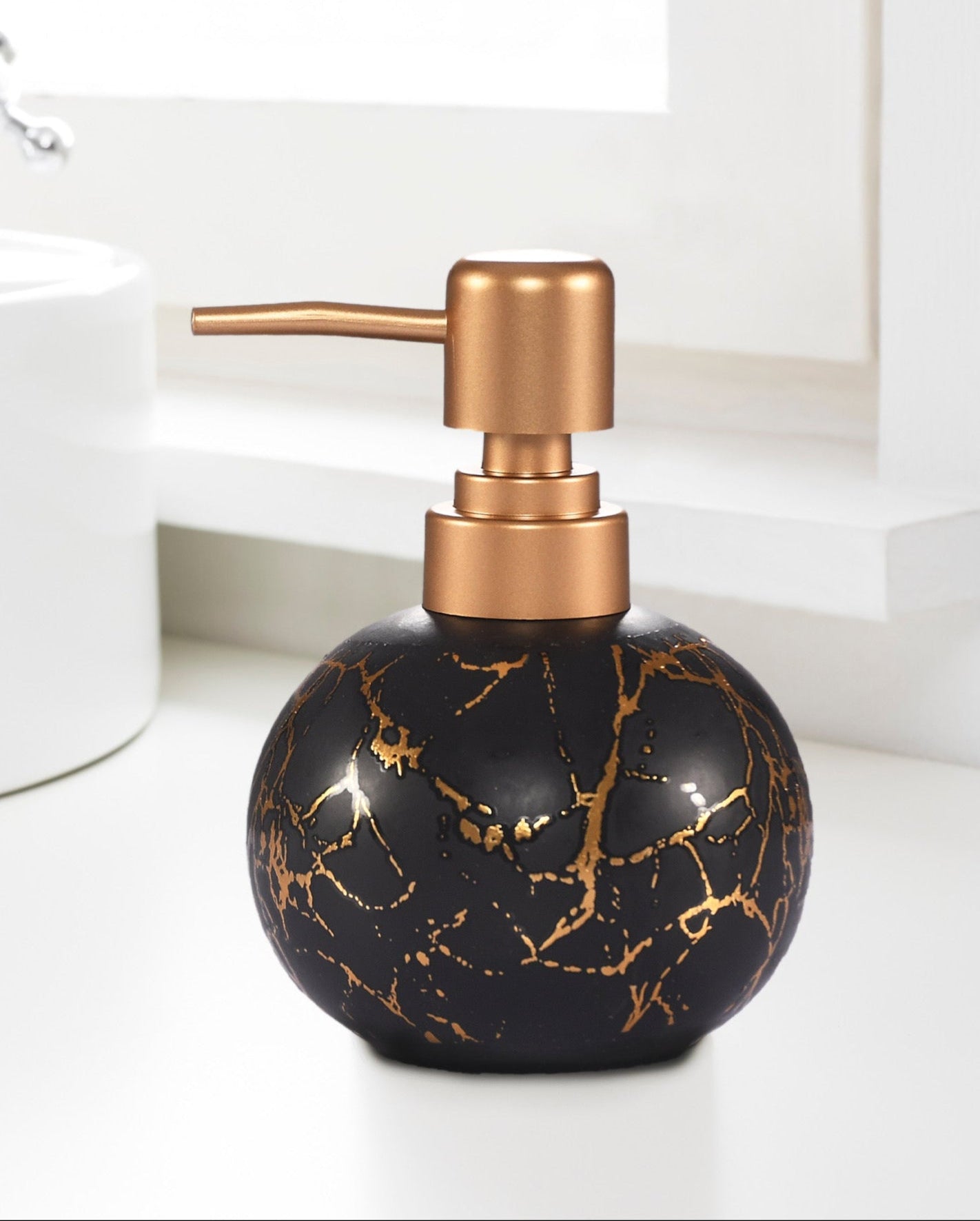 Black marble-patterned soap dispenser with copper pump on a bathroom counter.