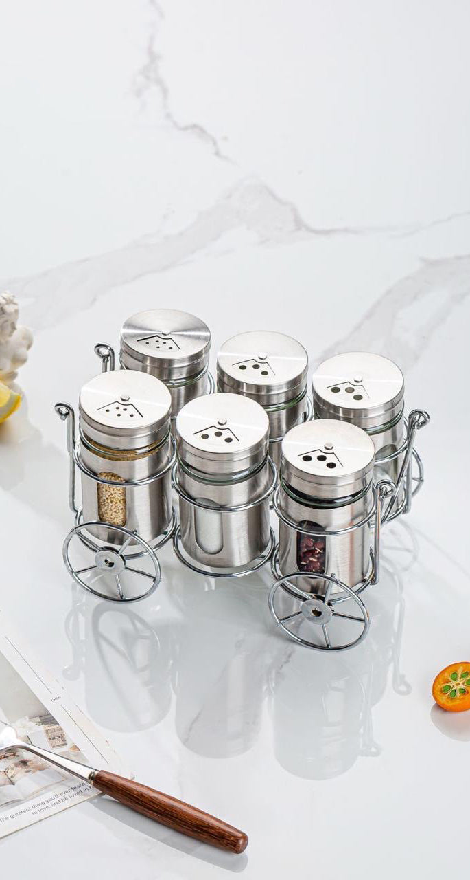 Set of metal spice jars on a marble surface with a fork and lemon.
